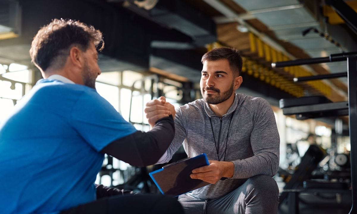 how to maintain fitness momentum during the holidays - coach gives manly handshake to a man inside a gym